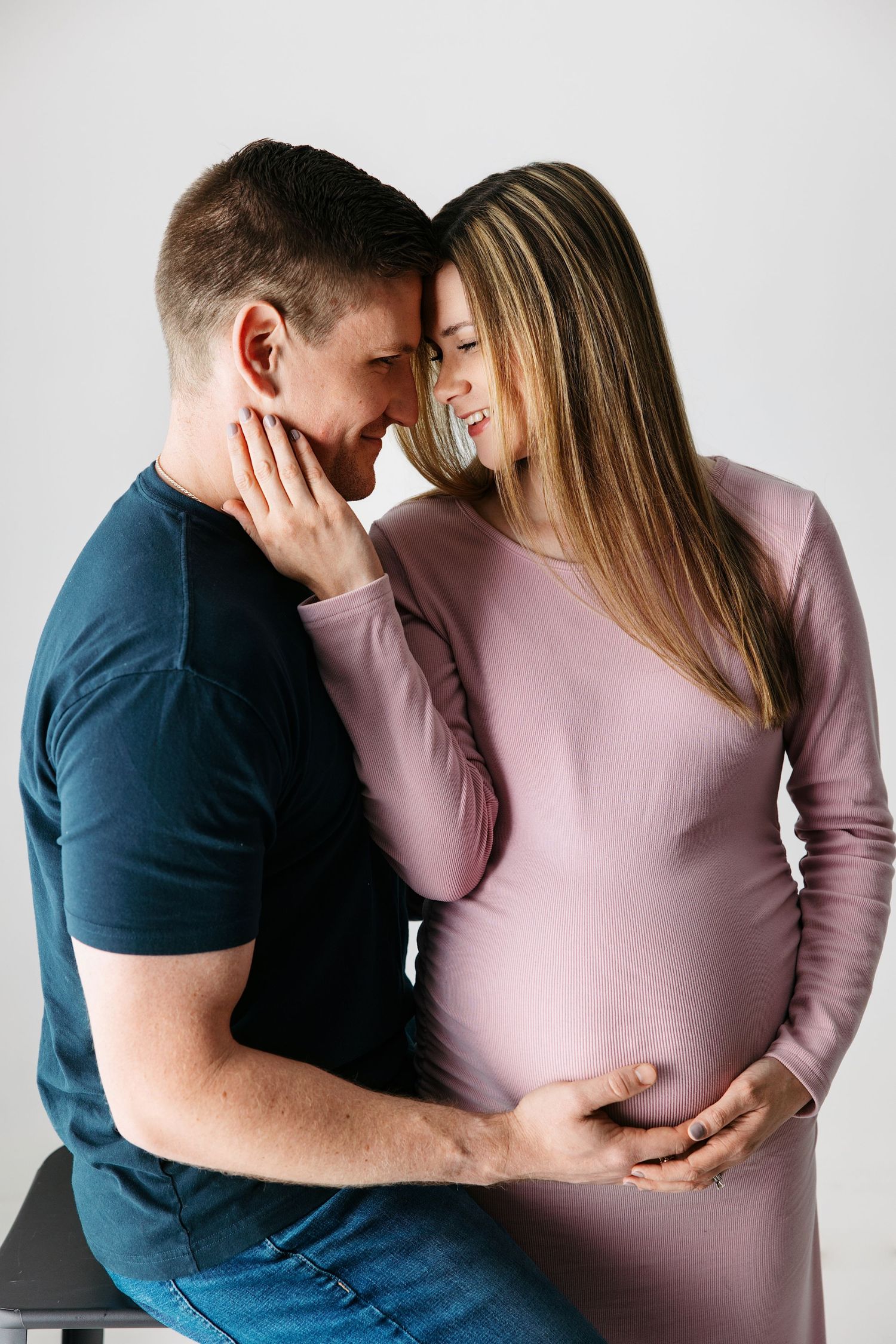 Expectant parents share intimate moments while celebrating pregnancy in a minimalist studio setting. Pleasant View maternity photographer