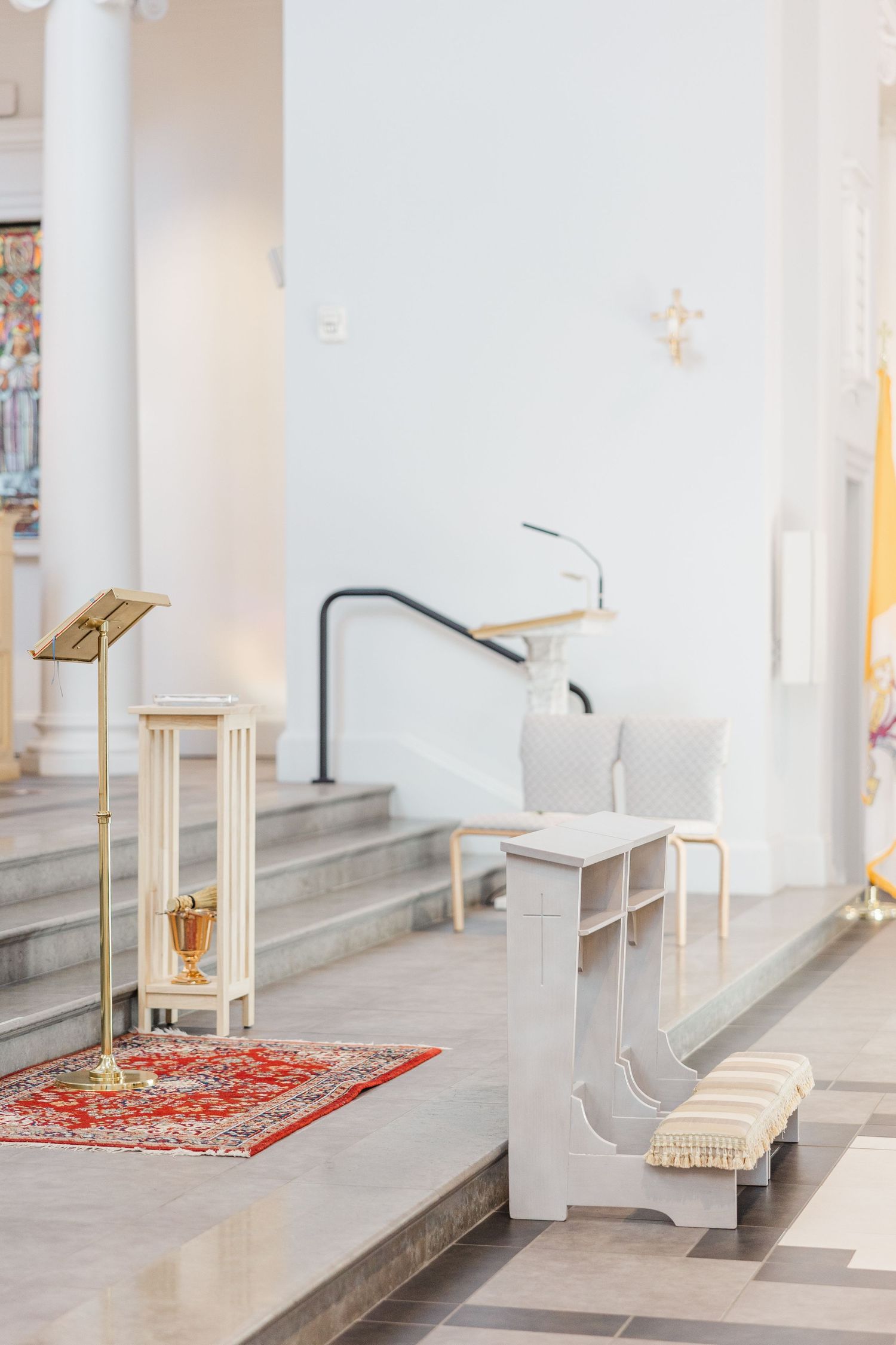 Interior view of a modern church with white walls, steps, and a decorative red carpet runner leading to the altar area.