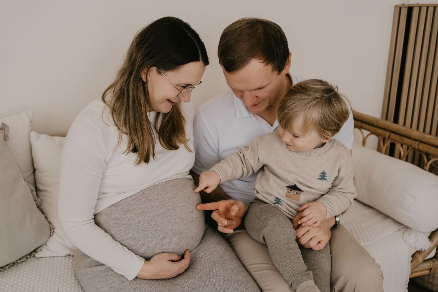A family sits together on a light gray couch in a cozy living room, sharing a tender moment.