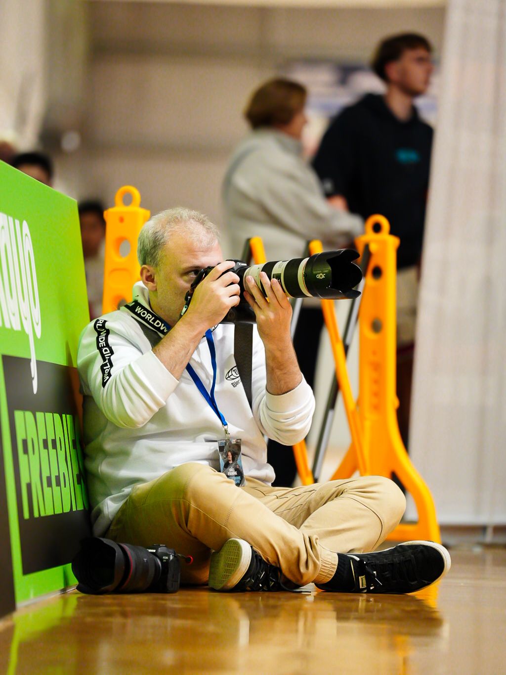 Photographers lying on hardwood floor capturing low-angle shots in studio.