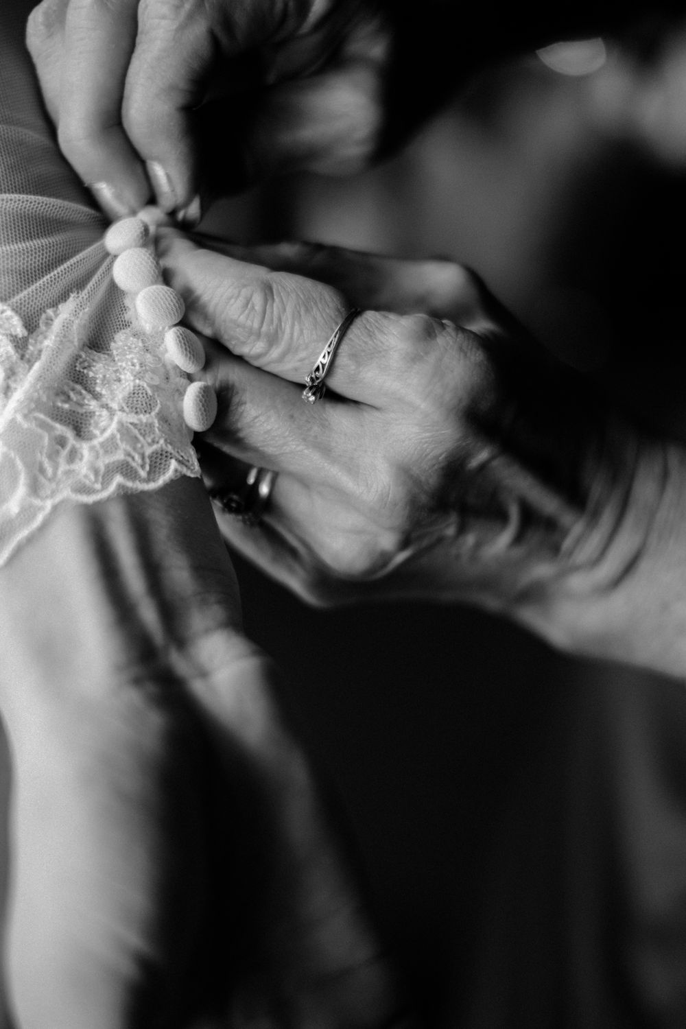 Mother of bride hands buttoning daughter's dress.