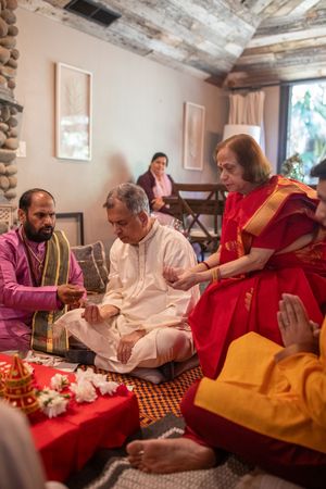 Traditional Hindu ceremony with participants in colorful attire seated on floor during religious ritual.
