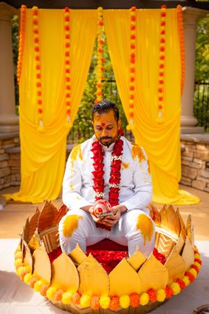 Traditional Indian wedding ceremony setup with bright yellow drapes and marigold garlands against stone wall backdrop.
