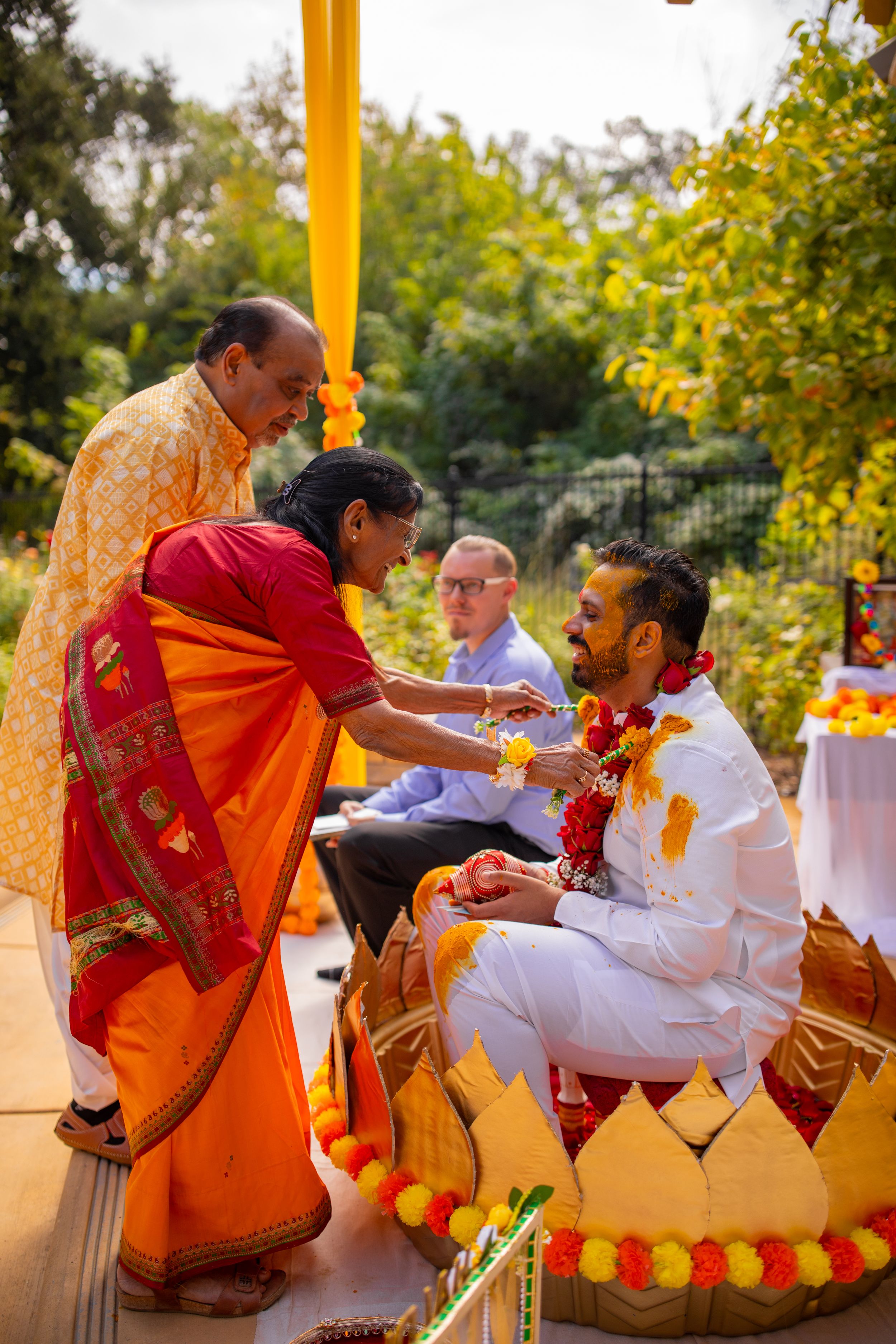 Traditional Indian wedding ceremony with guests exchanging blessings and gifts during a ritual under yellow canopy.