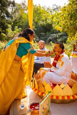 Wedding guests participate in a traditional Punjabi ceremony wearing yellow and white attire during an outdoor celebration.
