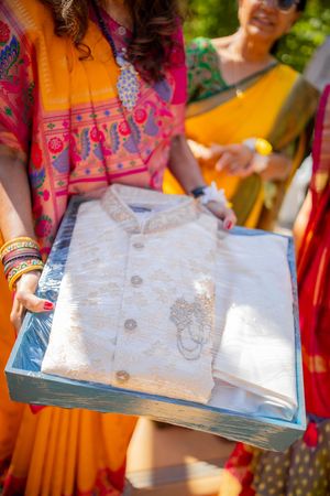 A person in orange and pink traditional attire holds up an open book or document in bright outdoor lighting.