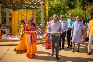 A group of people in traditional Indian attire gather outdoors under a covered walkway for a cultural celebration.