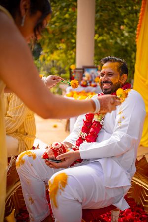 A person in white clothing relaxes on a decorated outdoor seat surrounded by red and orange floral garlands.