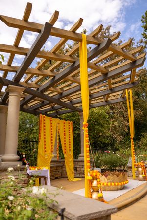 Wooden pergola decorated with bright yellow fabric draping creates an elegant outdoor event space in a garden setting.