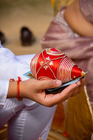 Hands holding a decorative red Christmas ornament with white swirls and patterns during a holiday celebration.