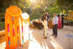 Colorful orange Indian wedding mandap decorated with flowers and garlands stands in golden sunlight at outdoor ceremony.