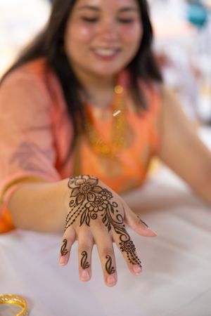 Close-up view of intricate henna designs being applied to a person's hand on a white surface.
