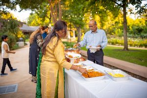 Guests enjoy an outdoor catered buffet line at sunset during a social gathering in a park setting.