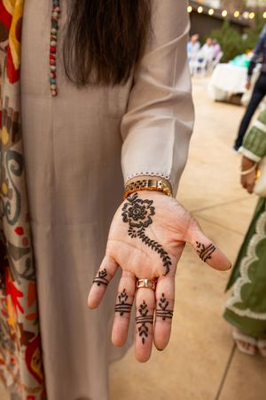 Several hands display intricate henna designs and temporary tattoos on their palms at a cultural event.