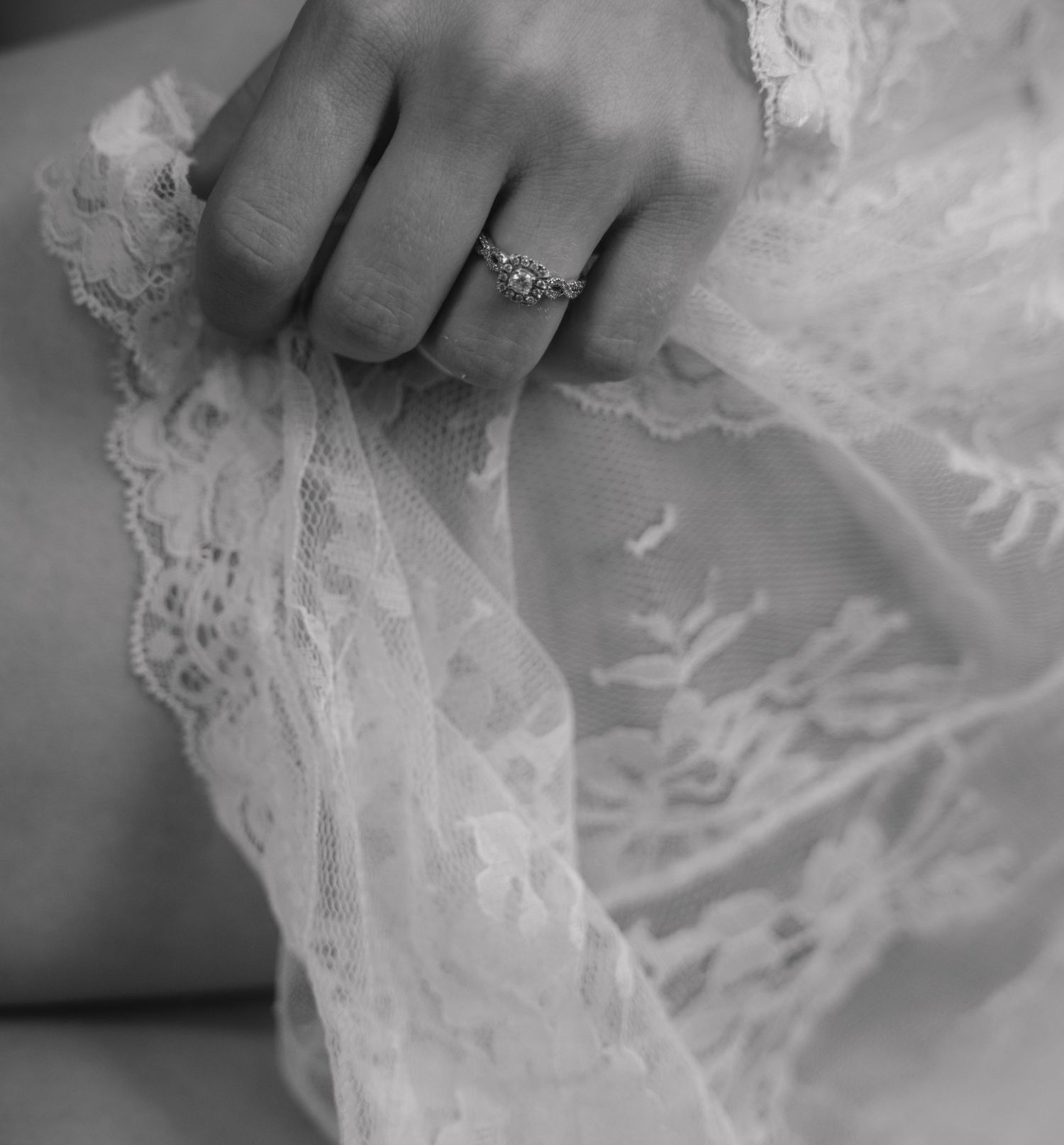 A black and white close-up of an engagement ring on delicate lace fabric.