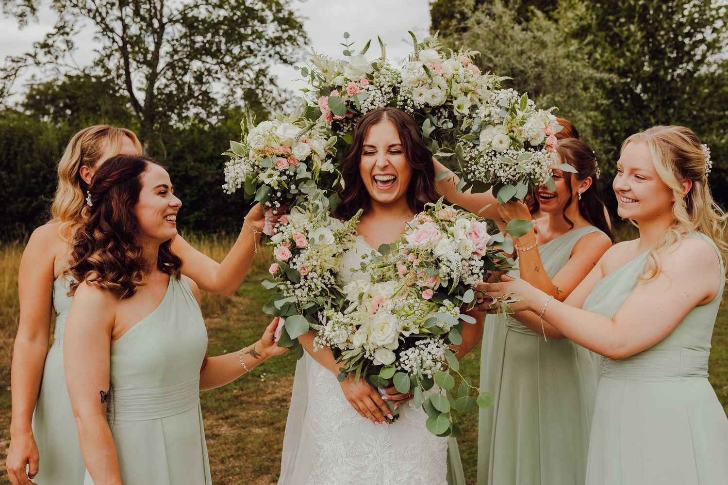 Bride surrounded by bridesmaids holding flower bouquets, joyful bridal party wedding photography