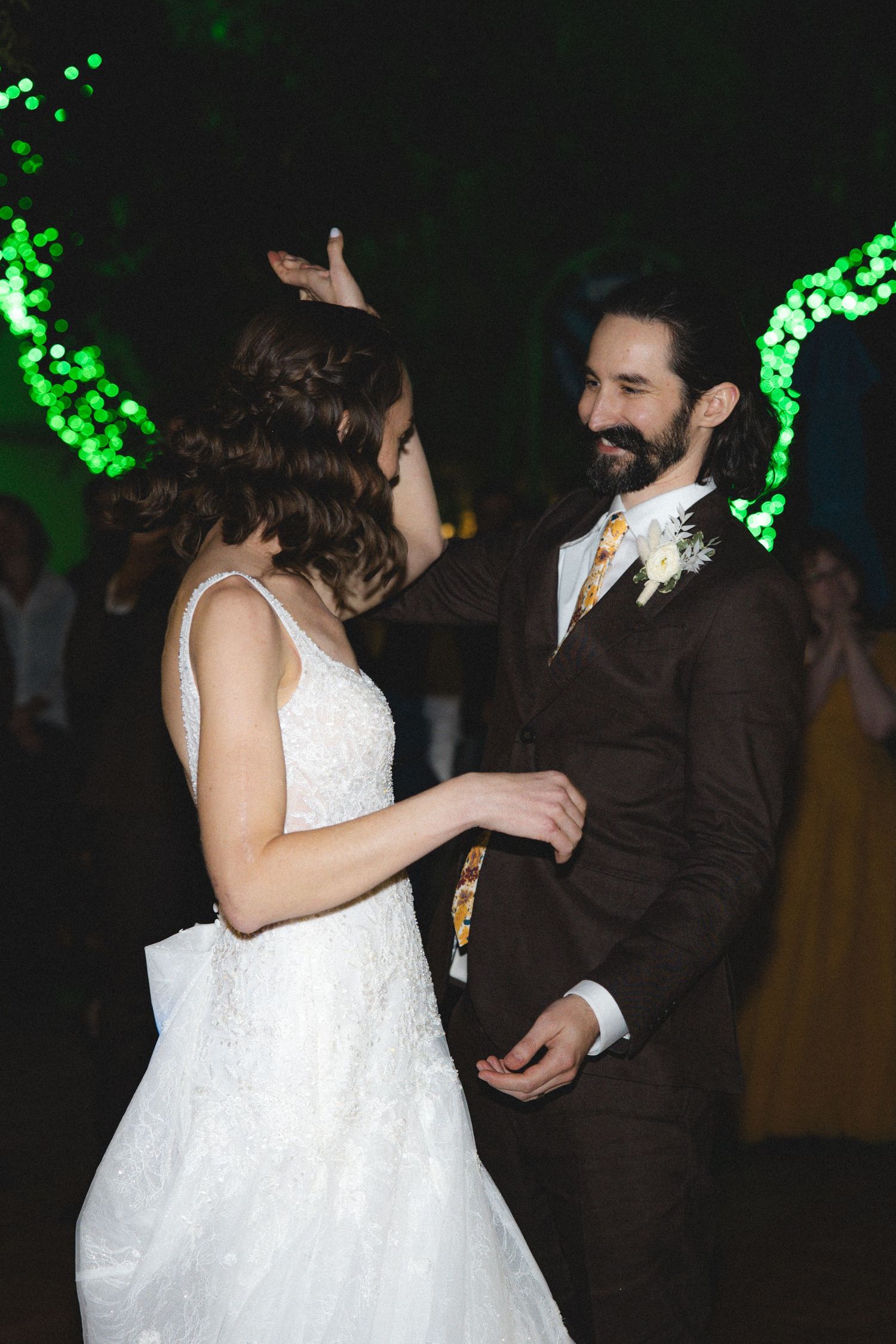 A couple dances together at a wedding reception with green bokeh lights glowing in the dark background.