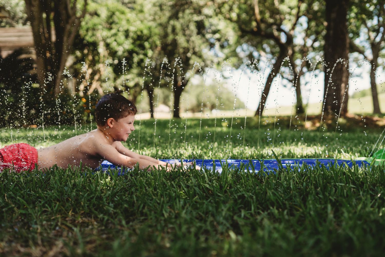 Child playing on a slip and slide in a grassy yard on a sunny day in Victoria, TX.