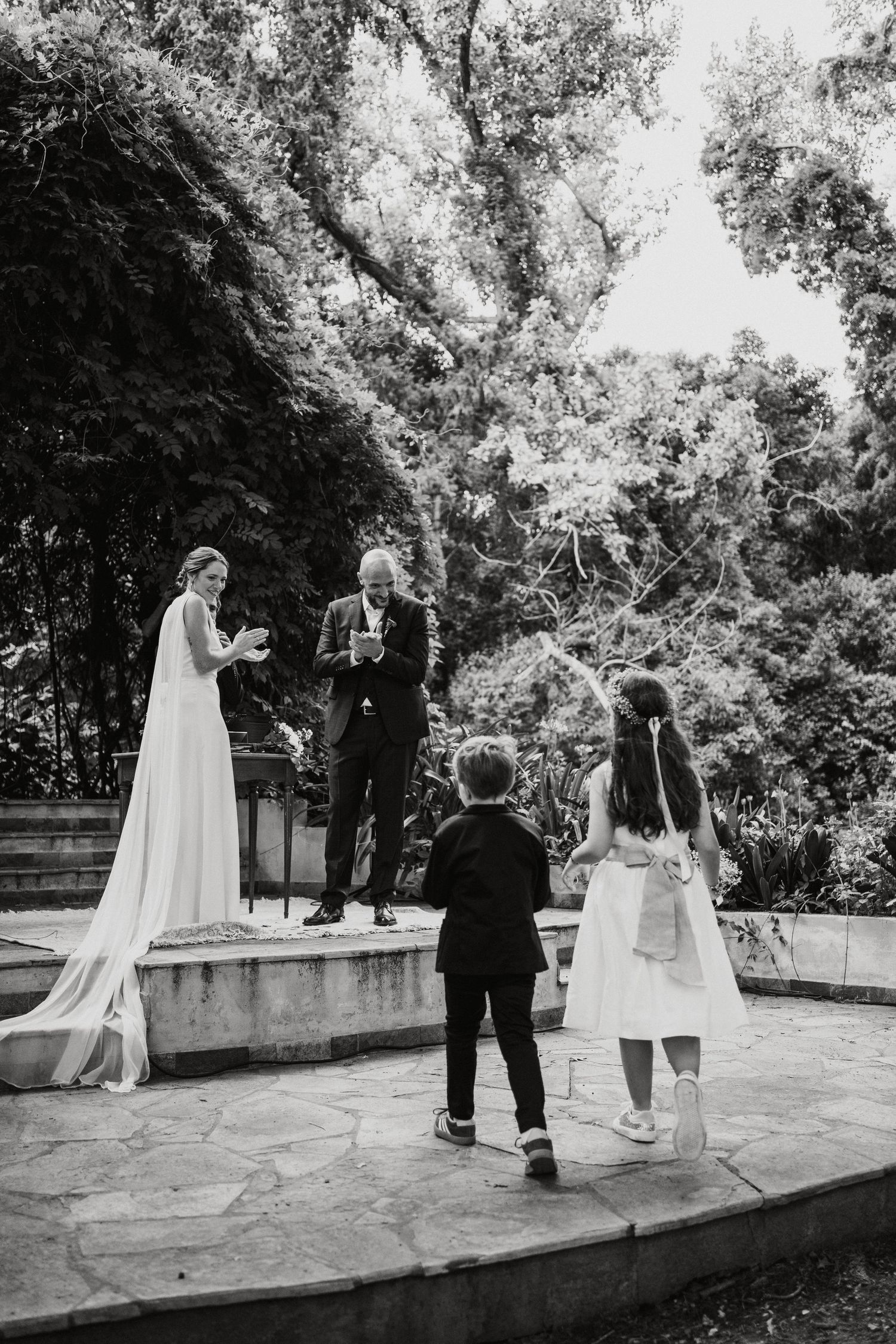 Black and white sequence of a couple dancing playfully on a concrete ledge in an outdoor garden setting.