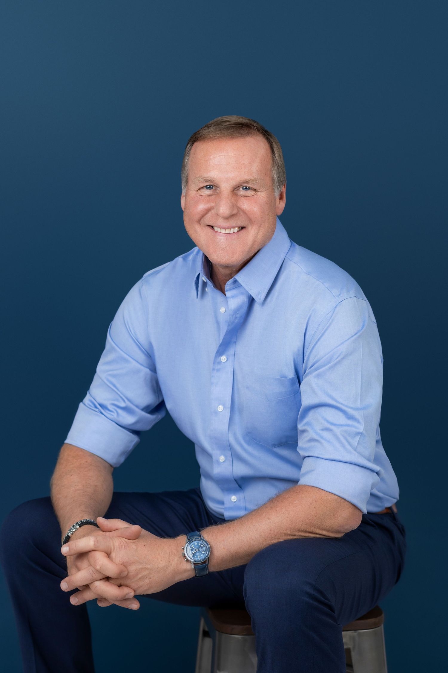 Professional headshot series of a person in a light blue dress shirt against a dark blue background.