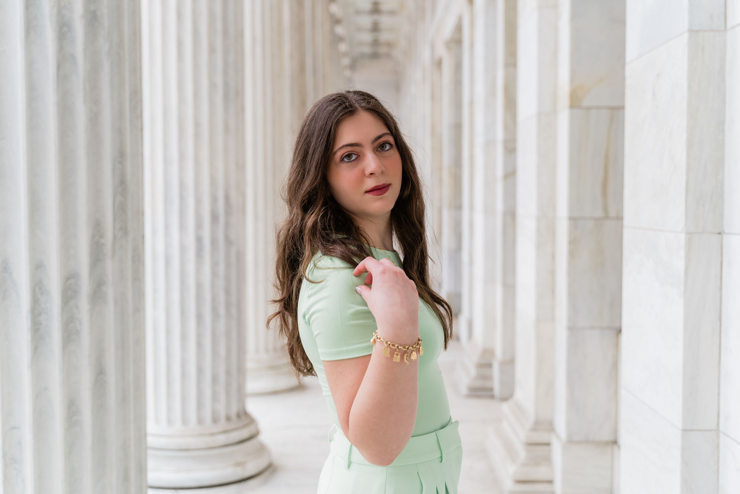 A woman in a mint green dress poses elegantly between white classical columns.