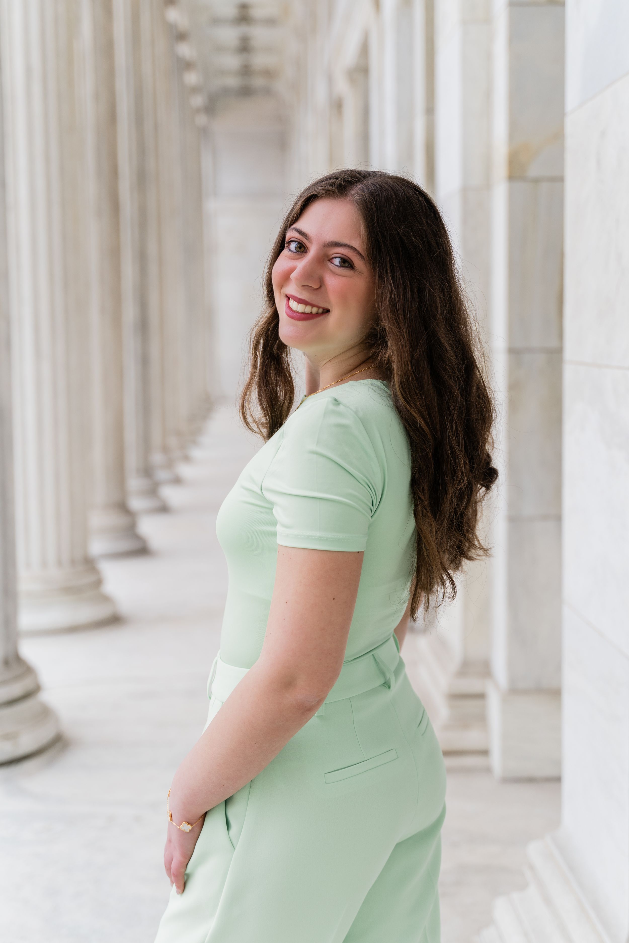 Woman in mint green t-shirt smiles and poses against white classical columns in an architectural setting.