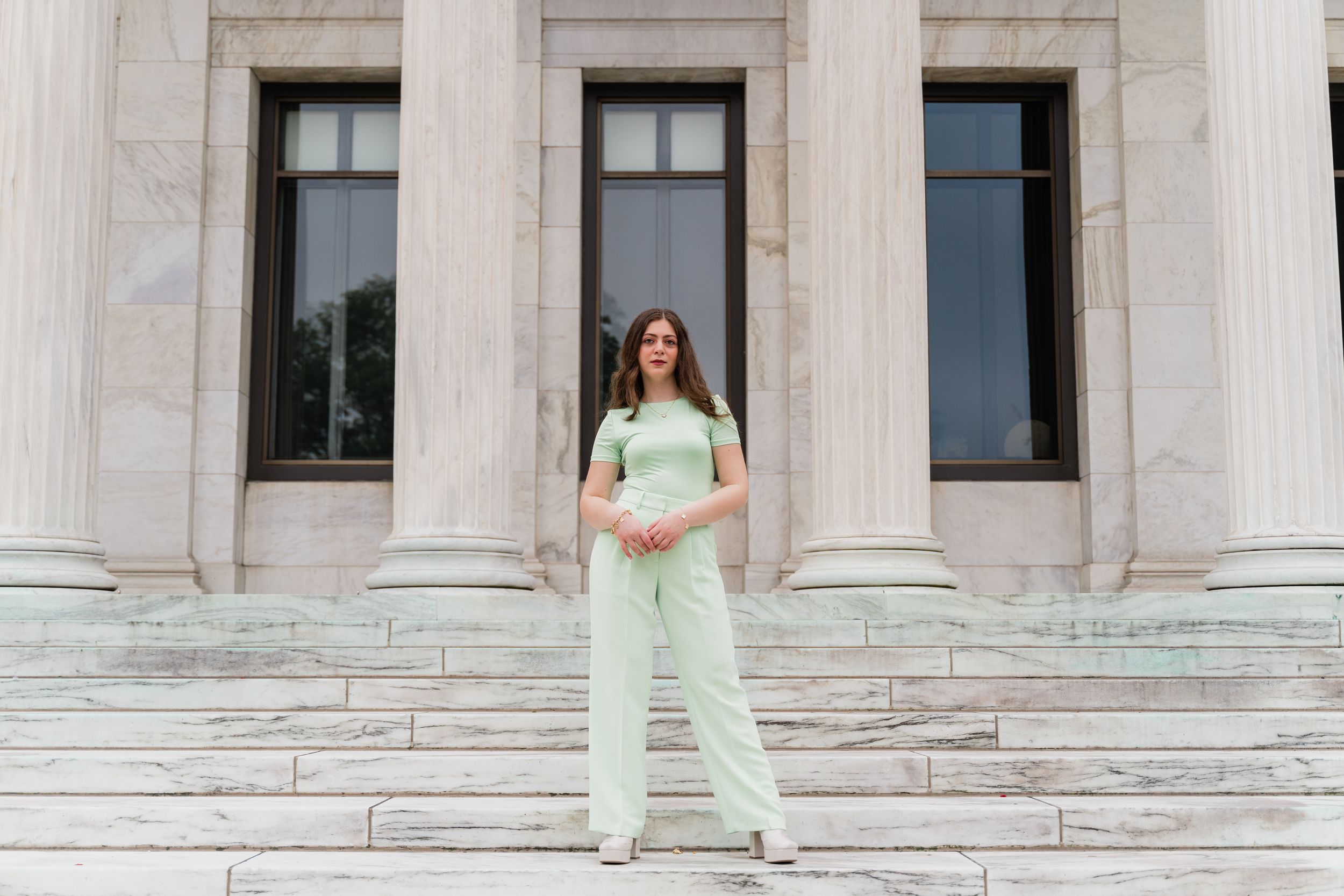 A person in mint green athletic wear poses on stone steps of a grand building with columns.
