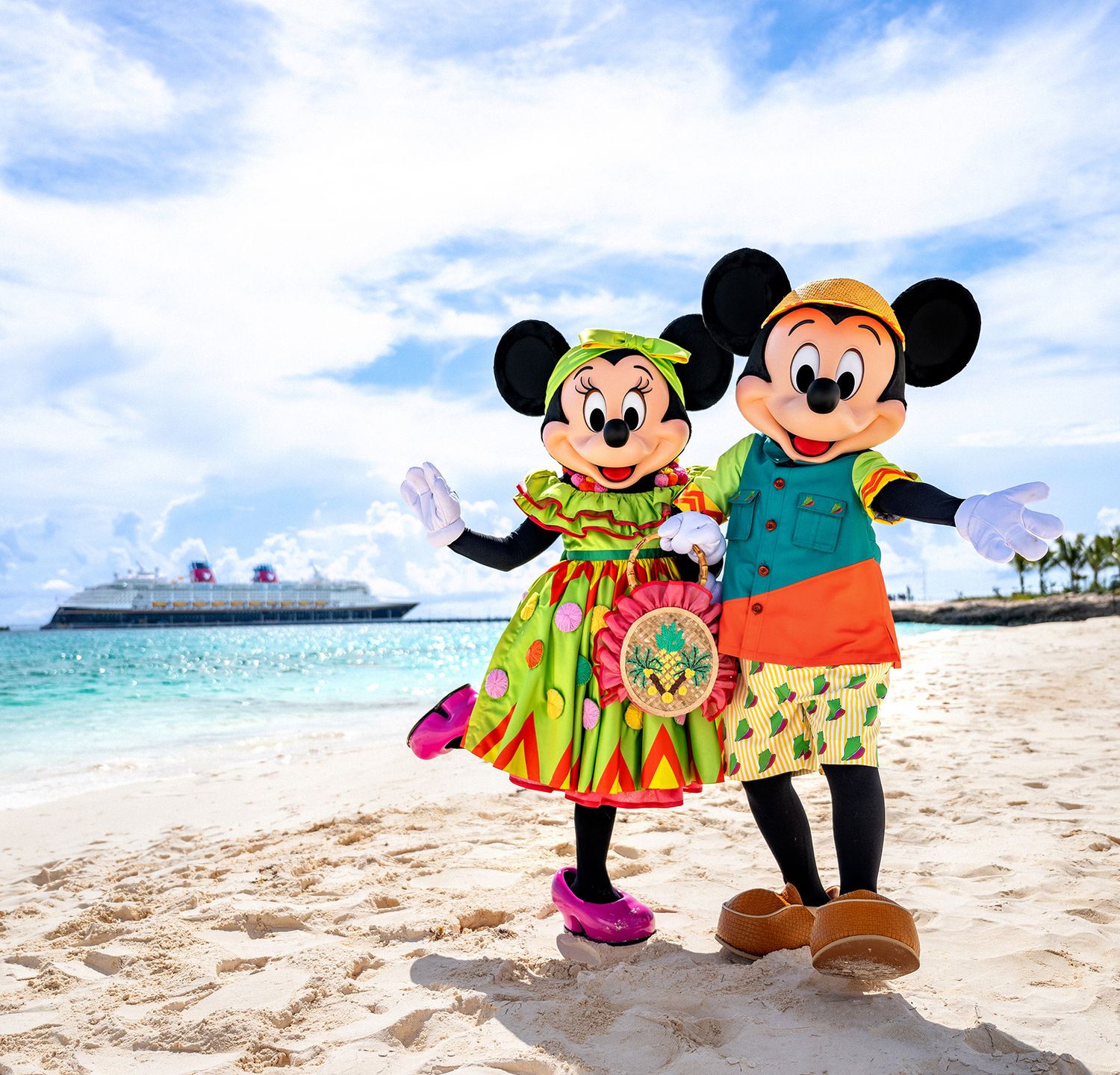 Disney characters Mickey and Minnie Mouse pose with guests on a beach with a Disney Cruise Line ship in the background.