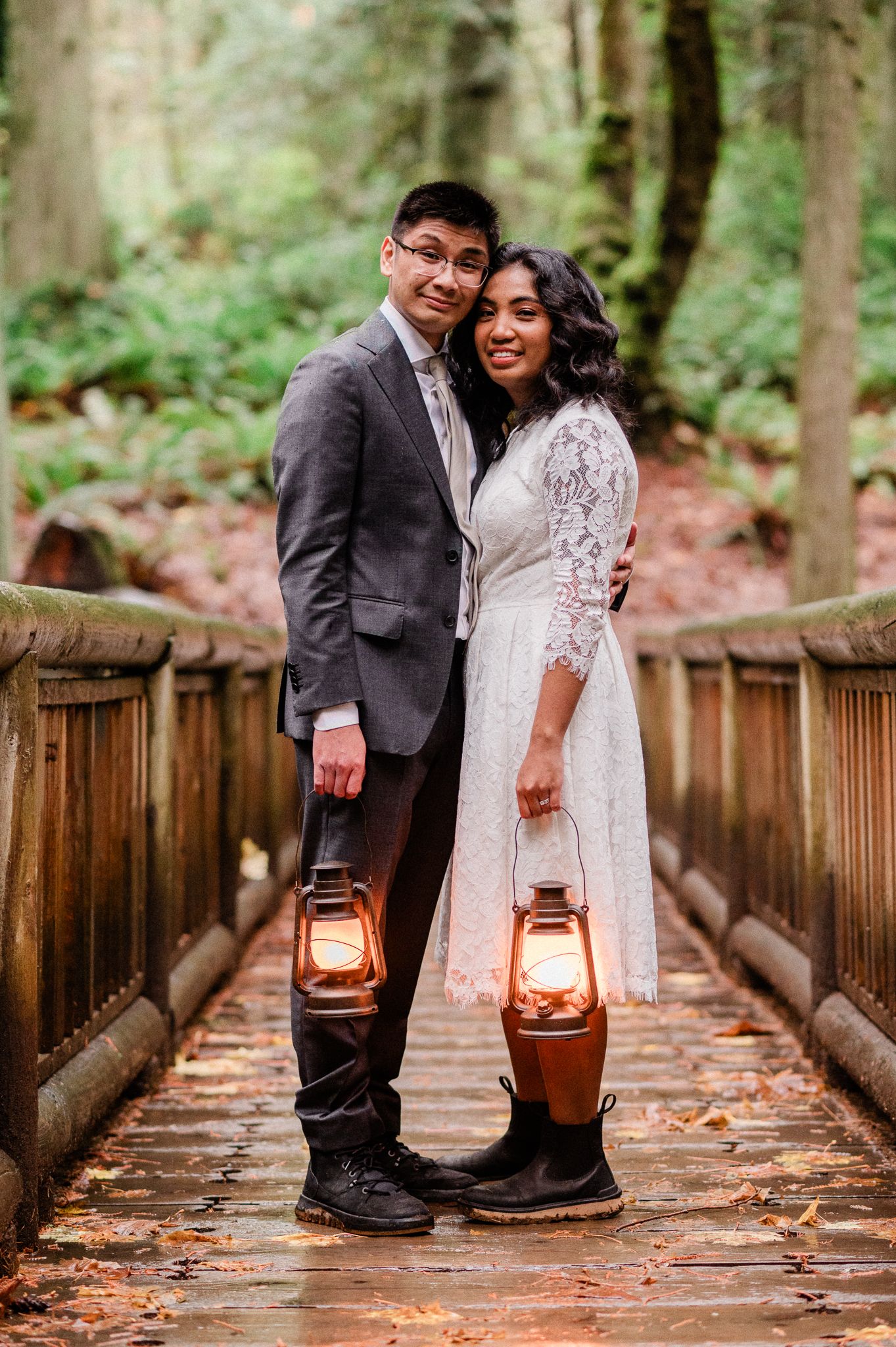A wedding couple holds vintage lanterns while standing on a wooden bridge in the Grand Forest West Trail for their elopement