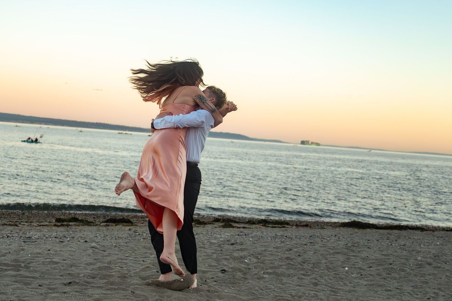 A romantic couple embraces on a beach at sunset with the ocean in the background.