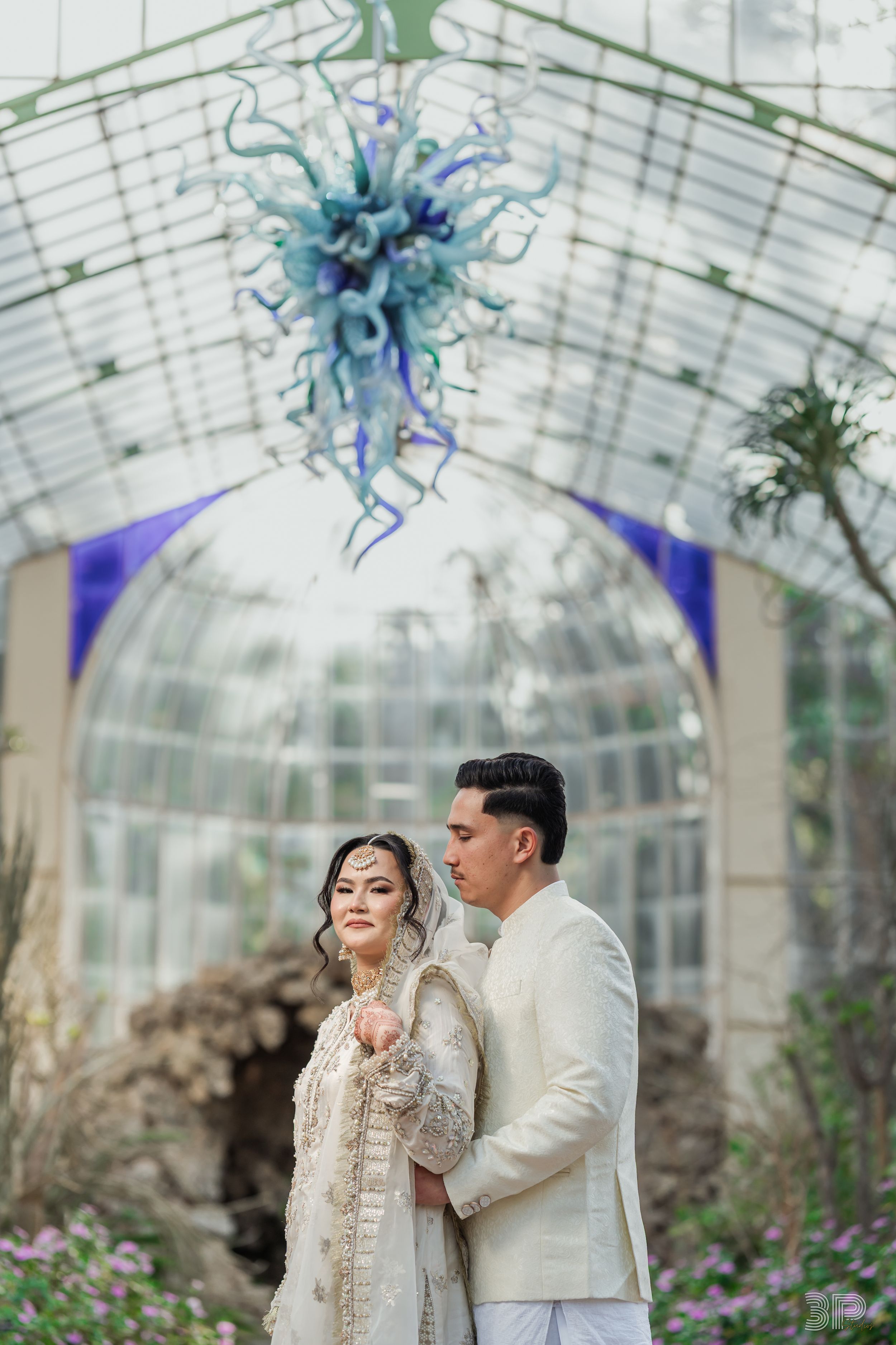 Elegant wedding ceremony setup in a glass conservatory decorated with hanging blue floral arrangements.