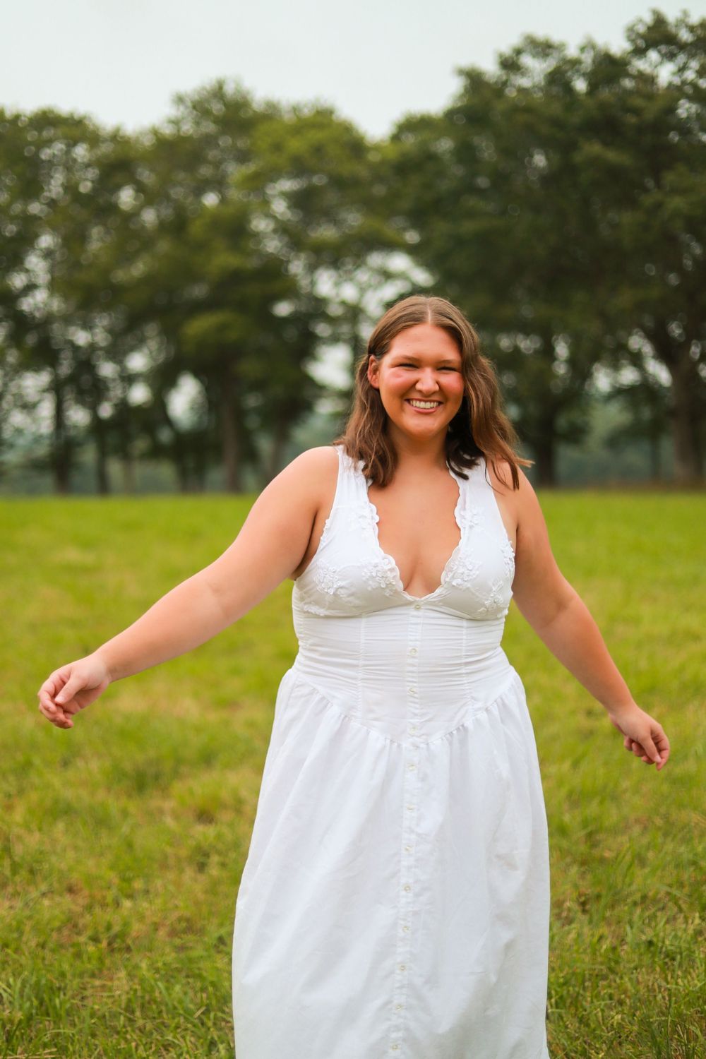 Person in flowing white dress twirls joyfully in grassy field.