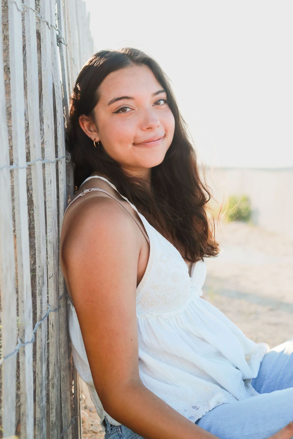 Person in white sleeveless top posing against weathered beach fence.