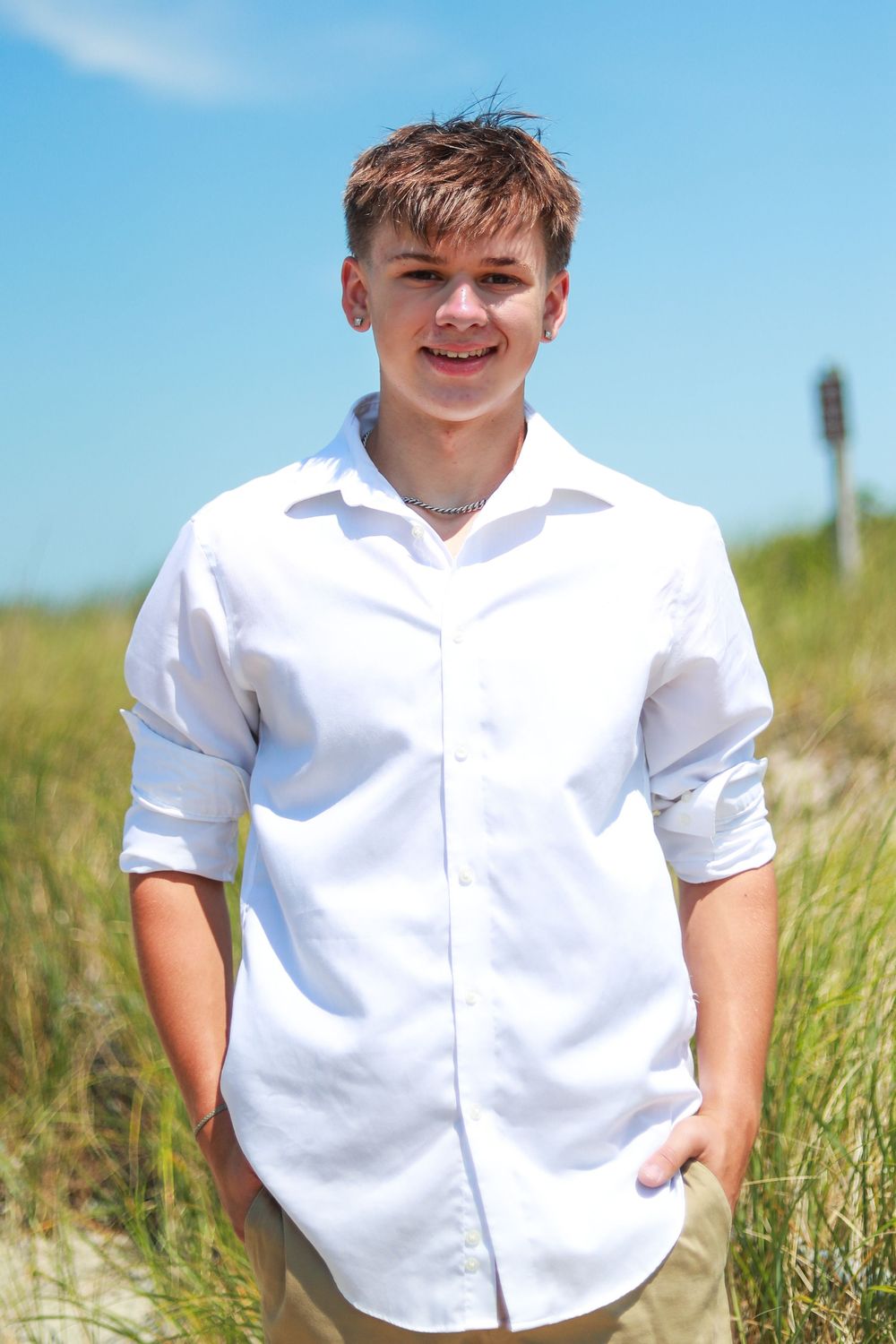 Portrait series in white button-down shirt against beach grass and blue sky.