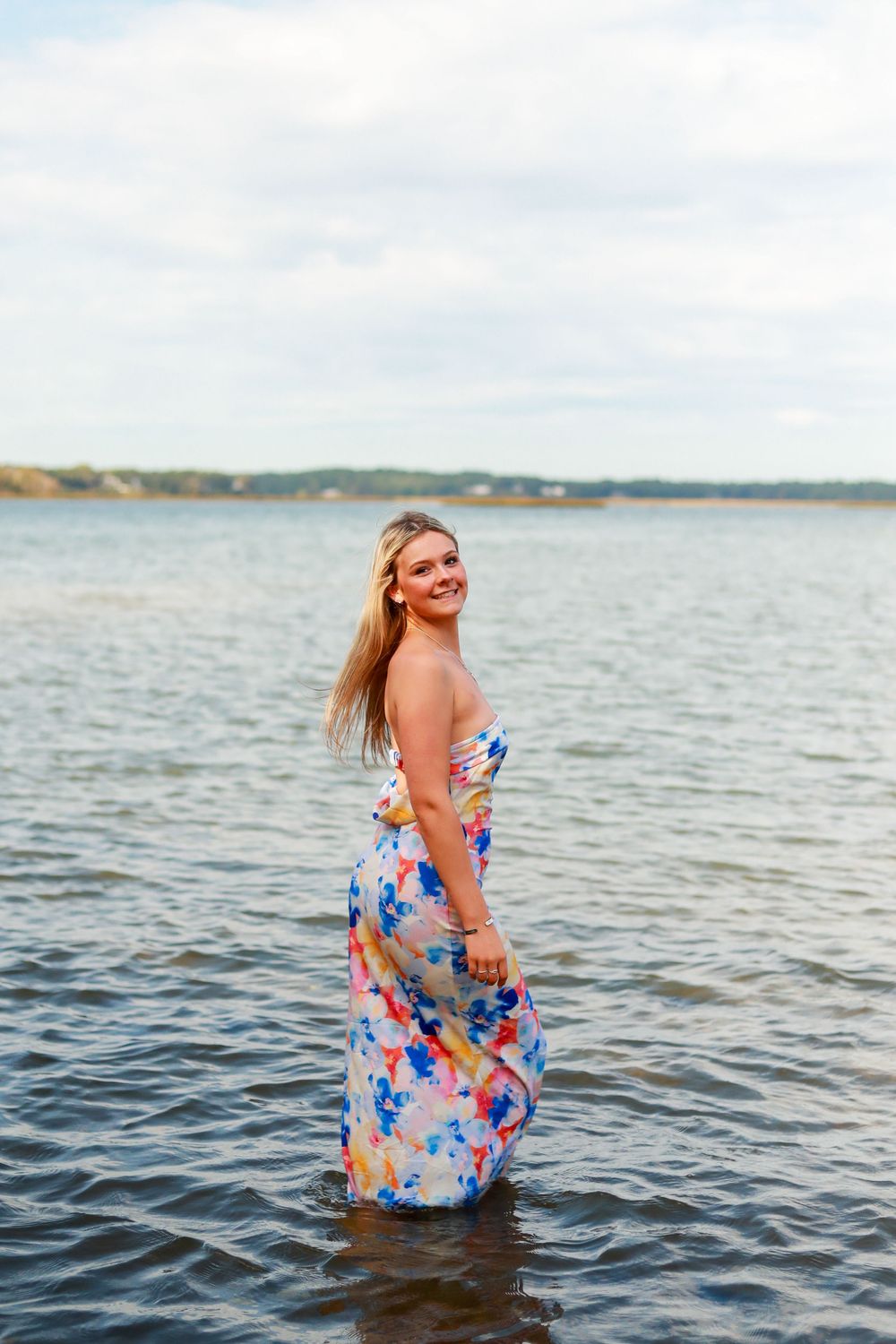 Person in floral dress standing in water during sunset at lake or ocean.