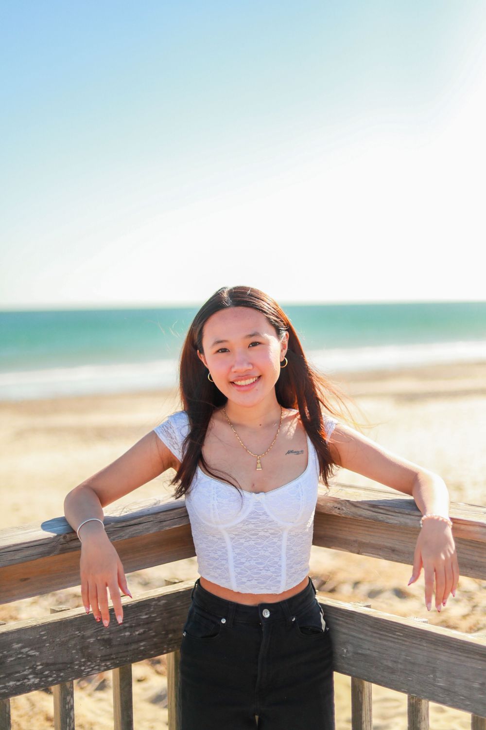 Person in casual attire poses along wooden beach railing at sunset.
