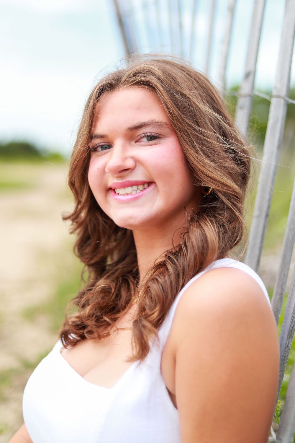 Person in white top poses against wooden fence at beach.