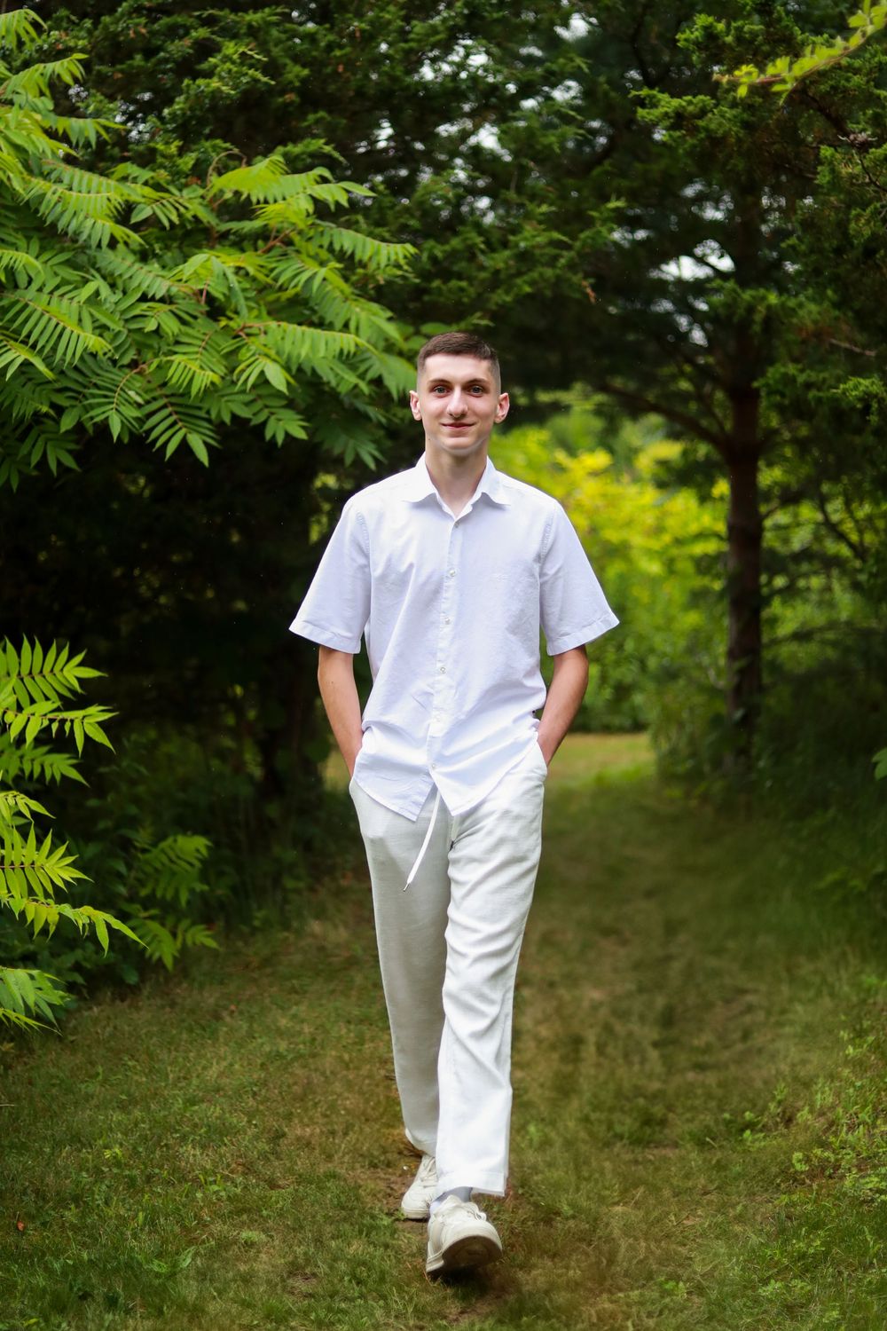 Person in white outfit walks through lush green garden path.