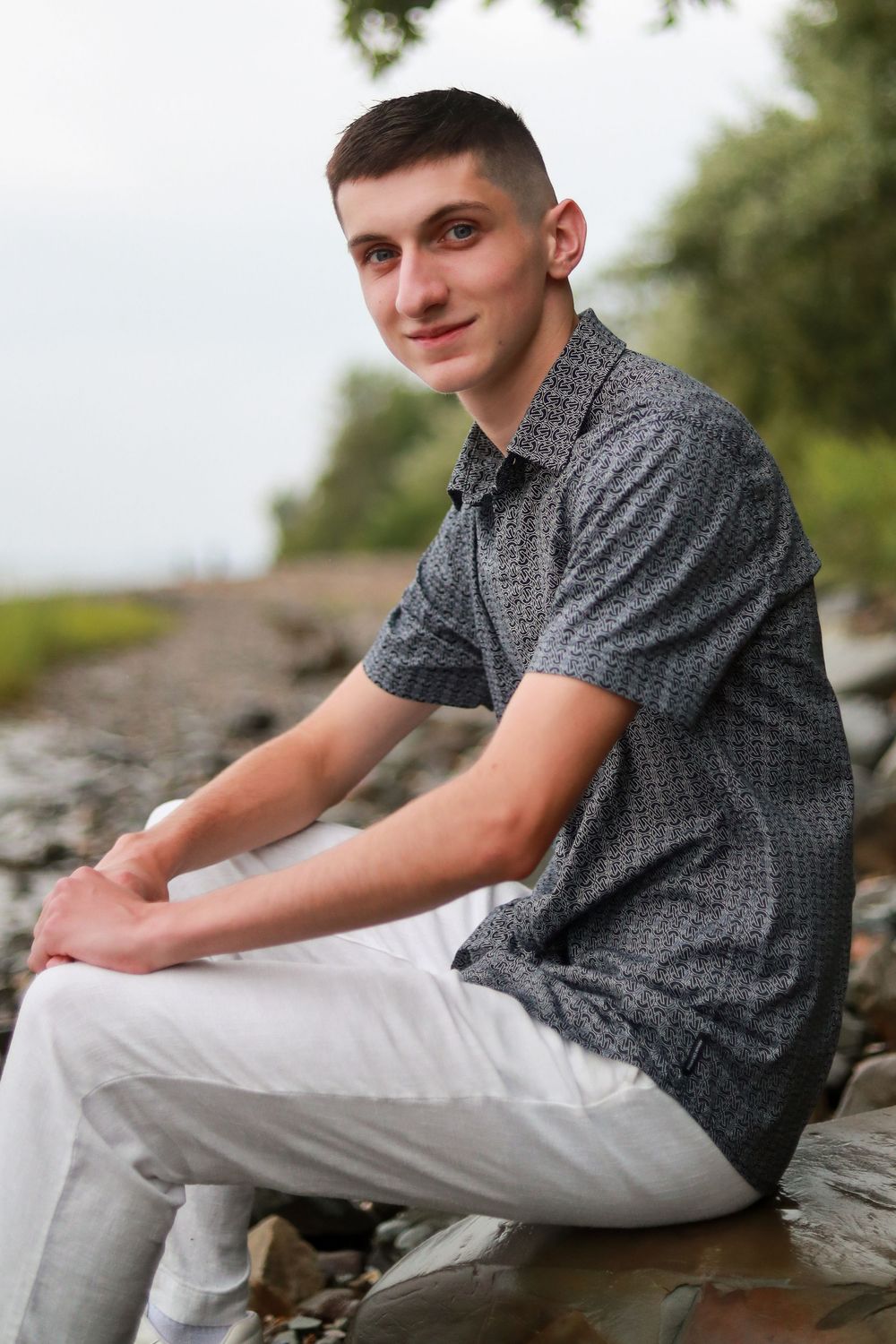 Young person in grey shirt and white pants posing on rocky shoreline.