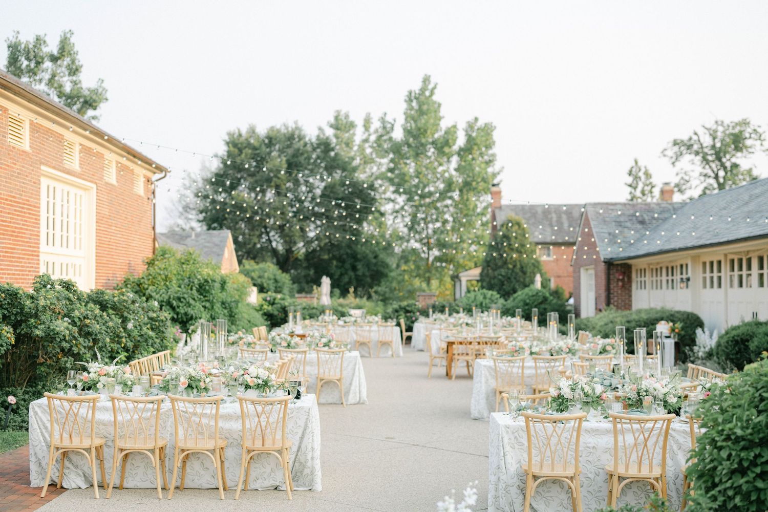 Elegant outdoor wedding reception setup with round tables, natural wood chairs and soft pastel decor under a sunny sky. - Elawa Farm