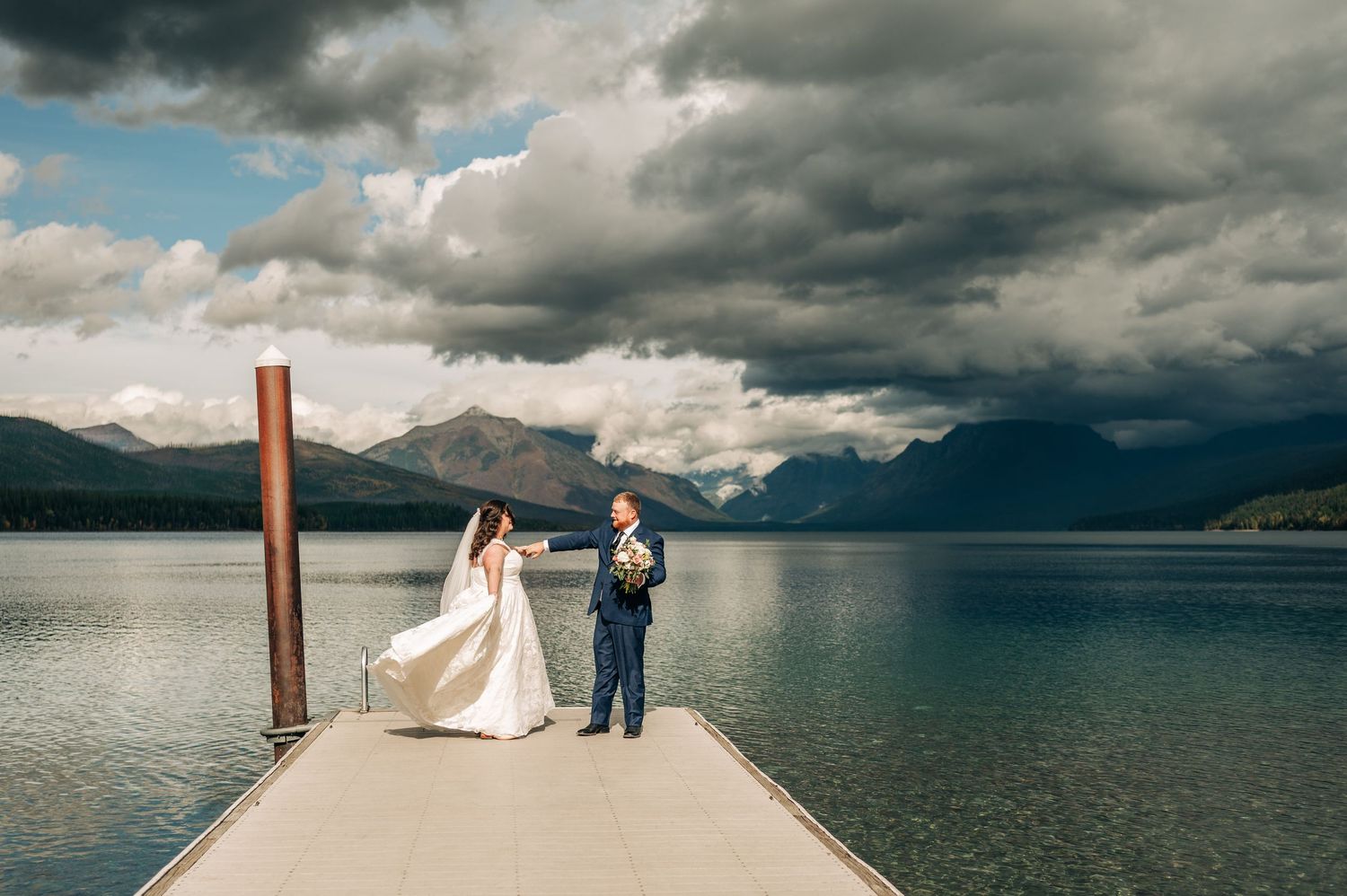 Wedding ceremony on a scenic dock overlooking a mountain lake with dramatic cloudy skies.