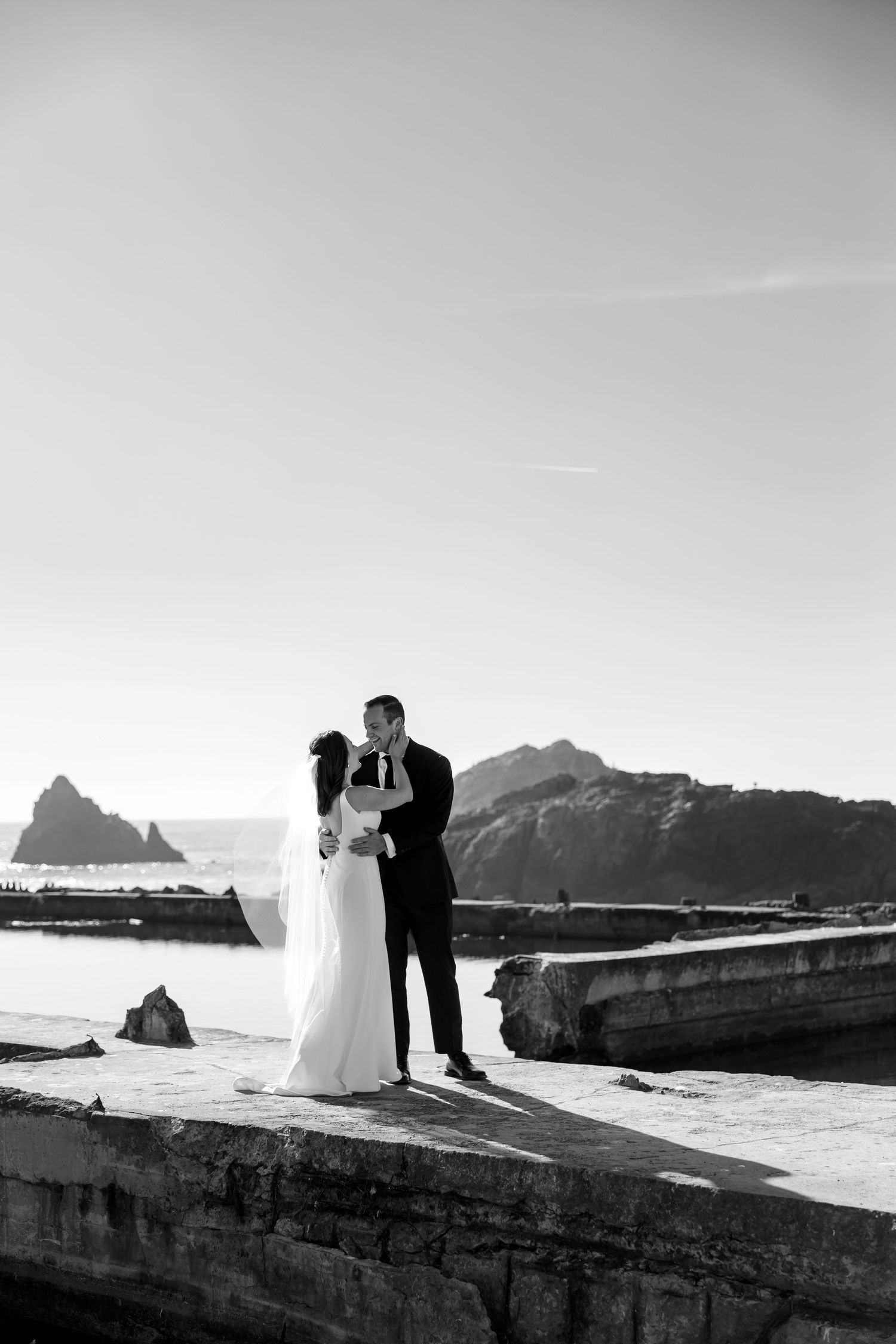 A romantic couple poses against dramatic coastal cliffs and ocean views in a series of black and white wedding photos at Sutro Baths.