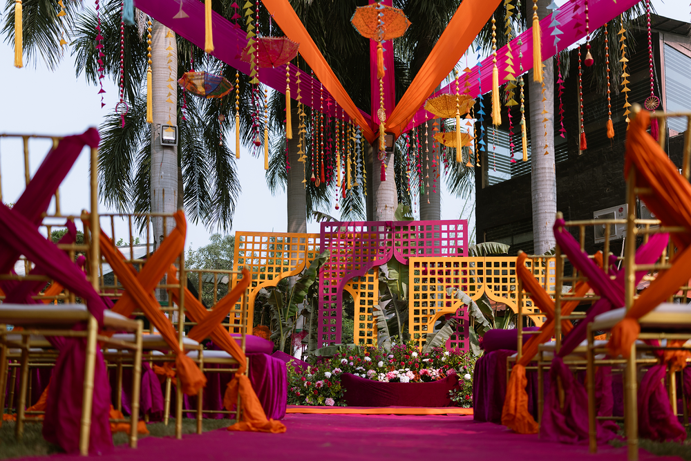 Vibrant pink and orange fabric decorations with hanging lanterns create a festive outdoor wedding venue setup.