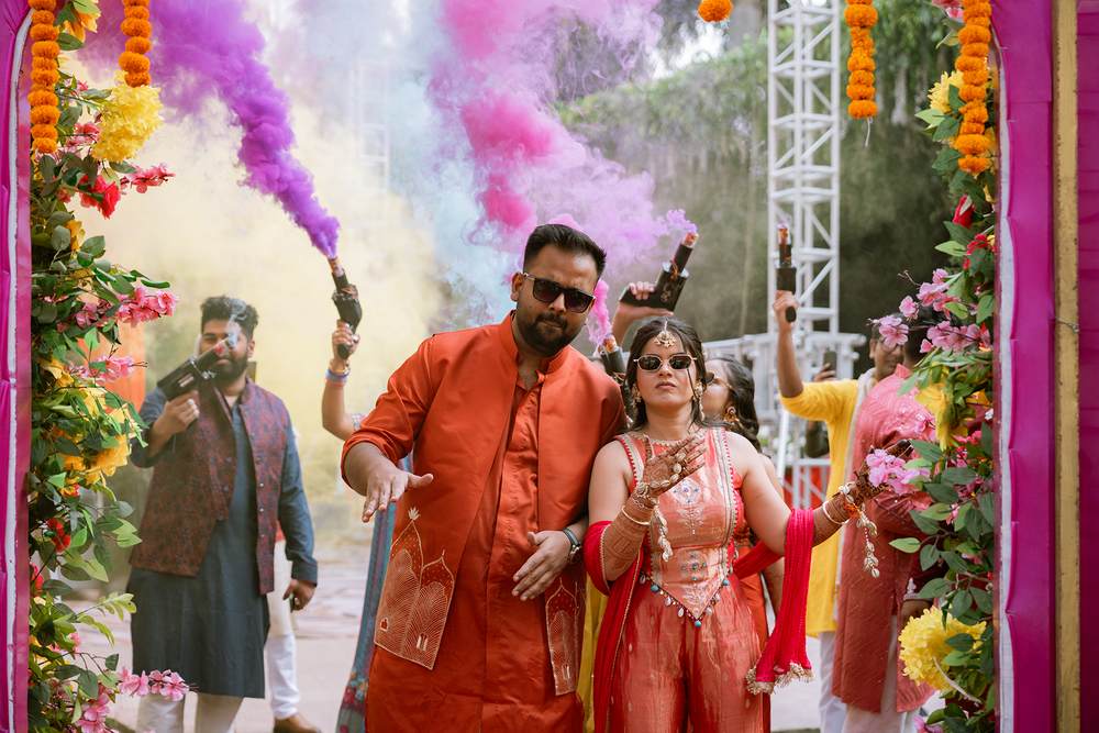 A vibrant Indian wedding ceremony with orange and purple floral decorations and guests in traditional attire.