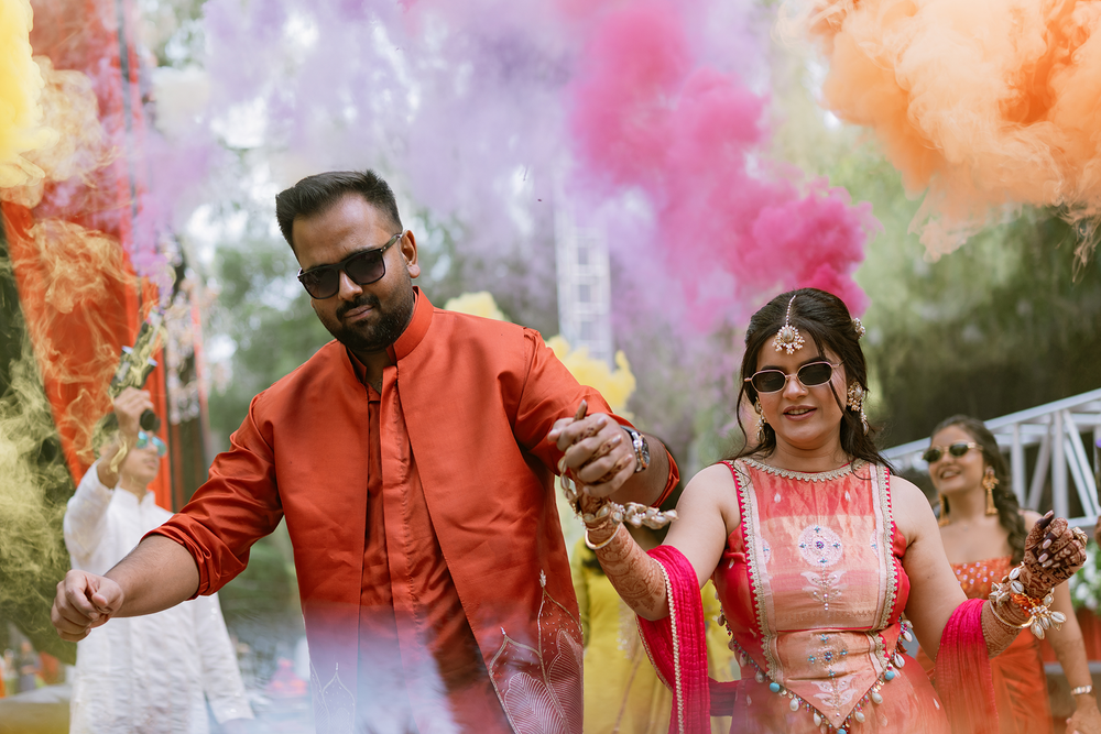 A couple celebrates with colorful smoke bombs and confetti during an outdoor engagement photoshoot.