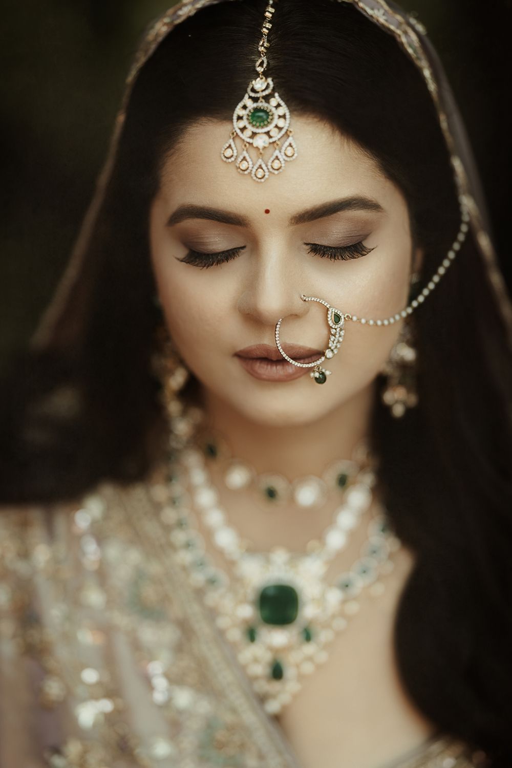 Close-up details of traditional Indian bridal jewelry and makeup featuring emerald stones and delicate nose ring adornments.