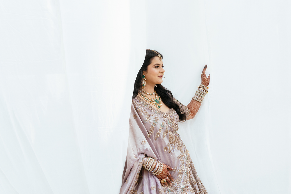 Woman in elegant light pink embroidered sari and traditional Indian bridal jewelry poses with phone.