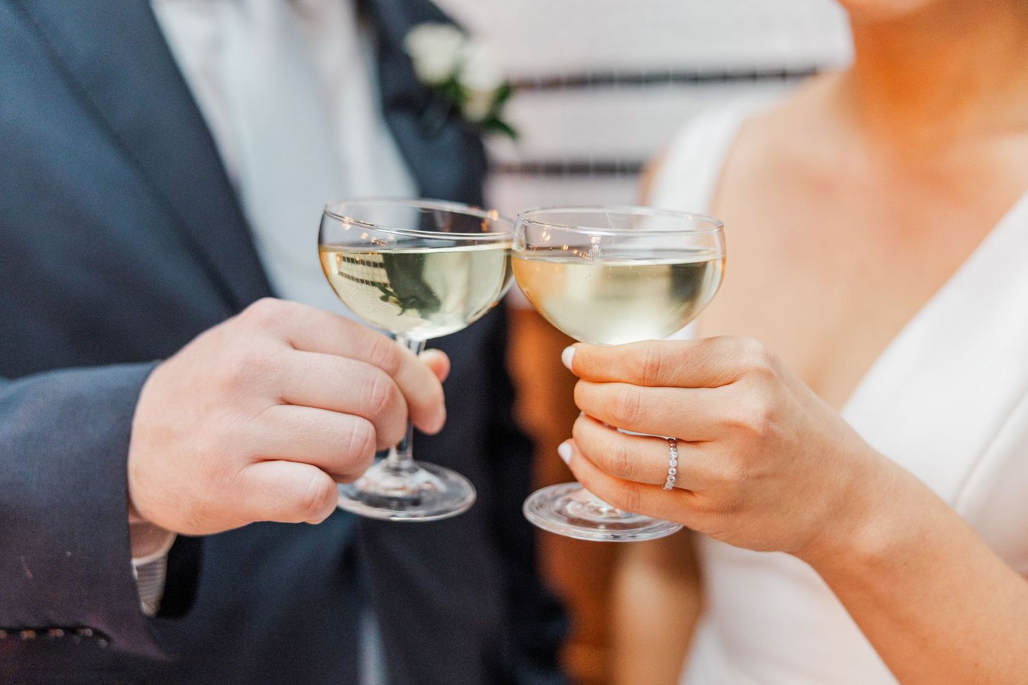 Hands clink champagne glasses together in celebration at an elegant event with soft lighting and floral decor.