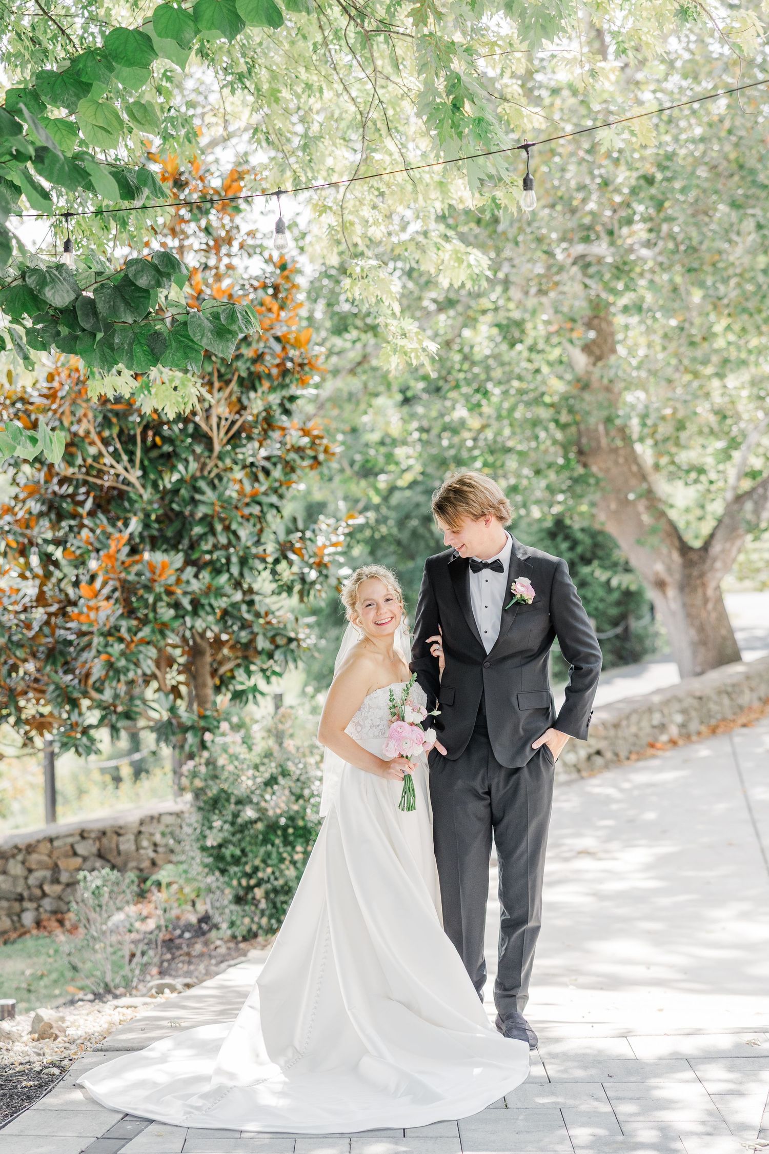 Bride and groom posing outdoors on stone steps with trees in the background.