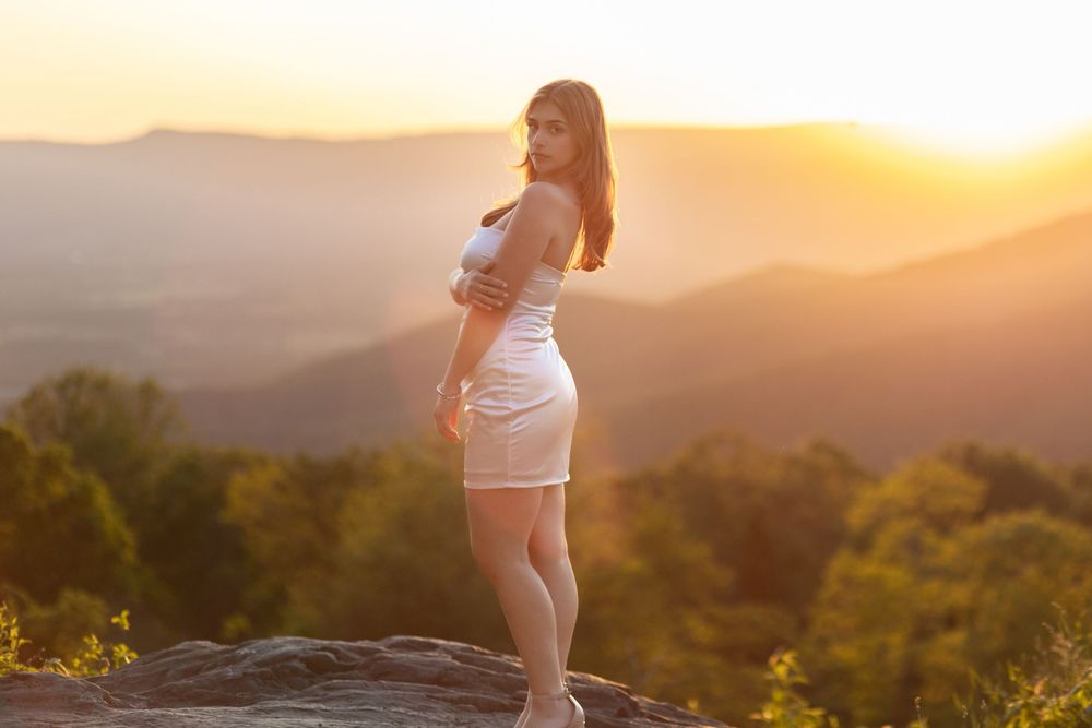 Silhouette of person standing on mountain ridge during golden sunset with rolling hills in background.